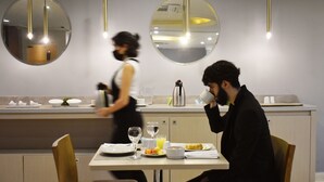 A modern dining area with a table set for two, a coffee maker, and a person sitting at the table. - Hotel Caribe 79 (Barranquilla)