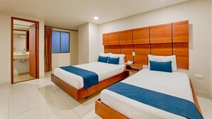 A hotel room with two beds, a wooden headboard, a bedside table with a lamp, and a bathroom visible through an open door. - Hotel Caribe 79 (Barranquilla)