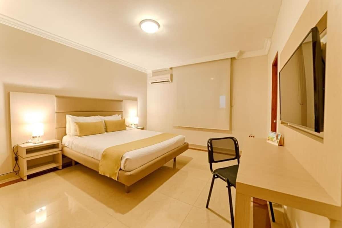 A hotel room with a bed, bedside tables, a chair, a desk, and a large mirror.