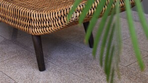 A wicker chair with a woven seat and backrest, positioned on a tiled floor. - Hotel Caribe 79 (Barranquilla)