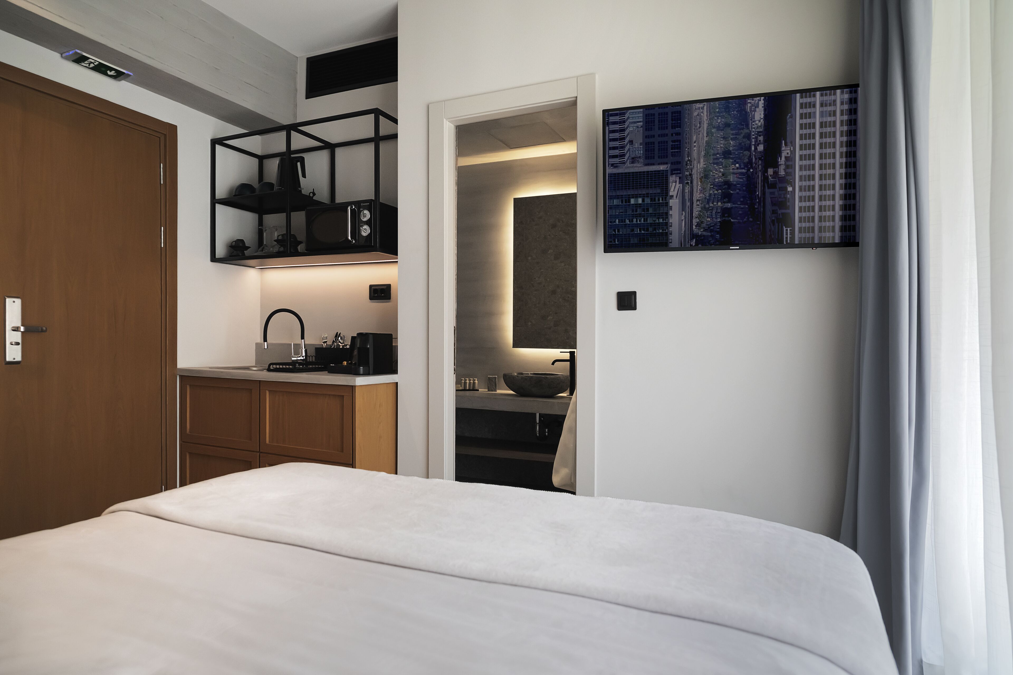 A modern hotel room with a large bed, a kitchenette with a microwave, and a cityscape painting on the wall.