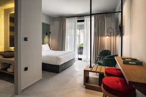 A modern hotel room with a bed, a wooden table, red chairs, a small seating area, and a view of the outdoors through large windows. - Bob W Athens Akadimia (Athens)