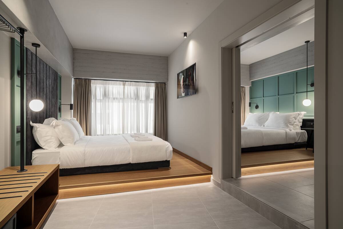 A modern hotel room with a large bed, a wooden bedside table, a mirror, and a view of the city.