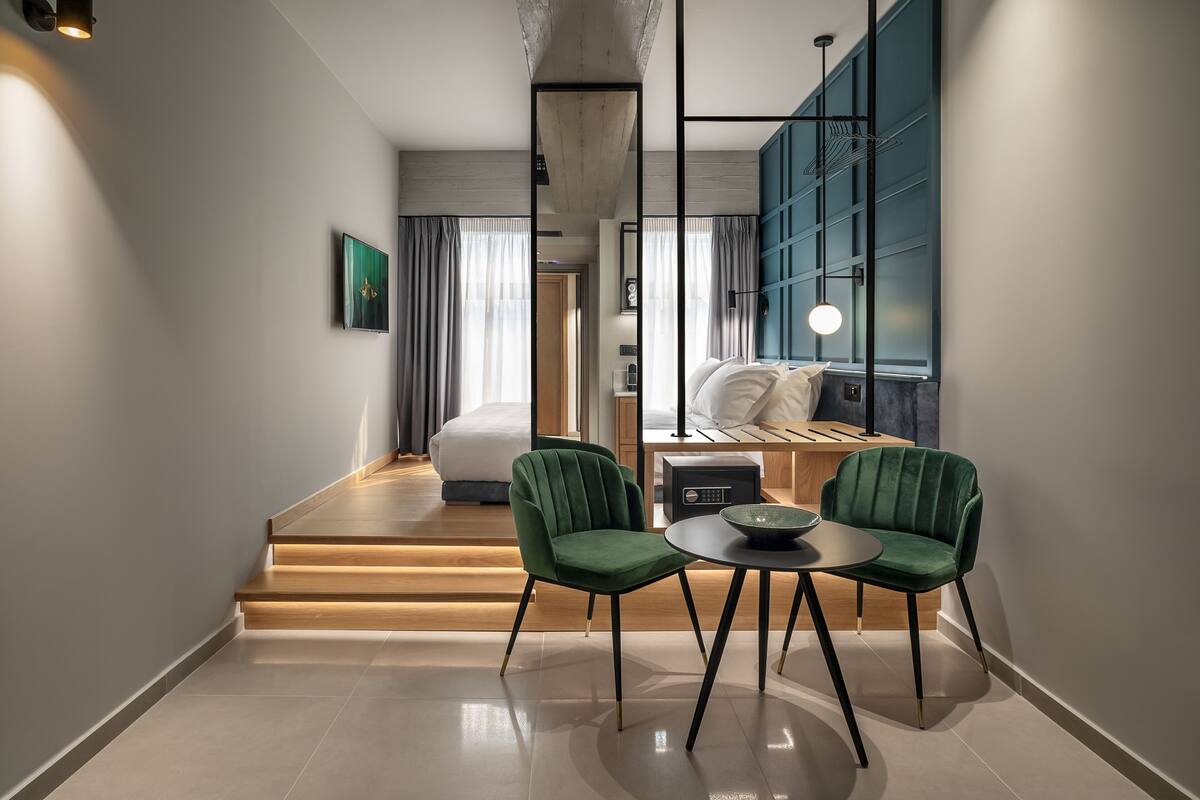 A modern hotel room with a bed, a desk, two chairs, a small table, and a view of the city.