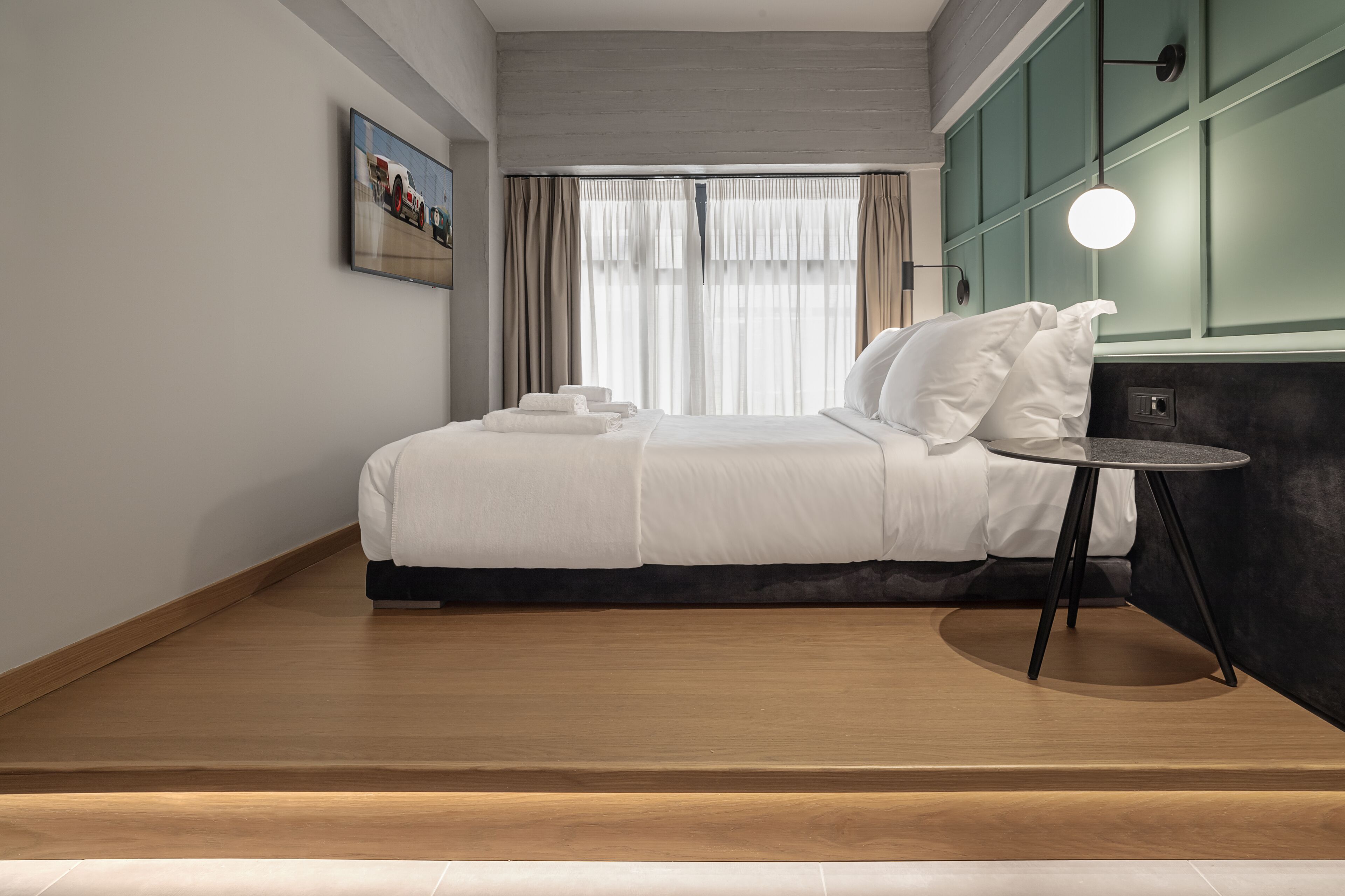 Ein modernes Hotelzimmer mit einem ordentlich bezogenen Bett, einem kleinen runden Tisch und einem Bild an der Wand.