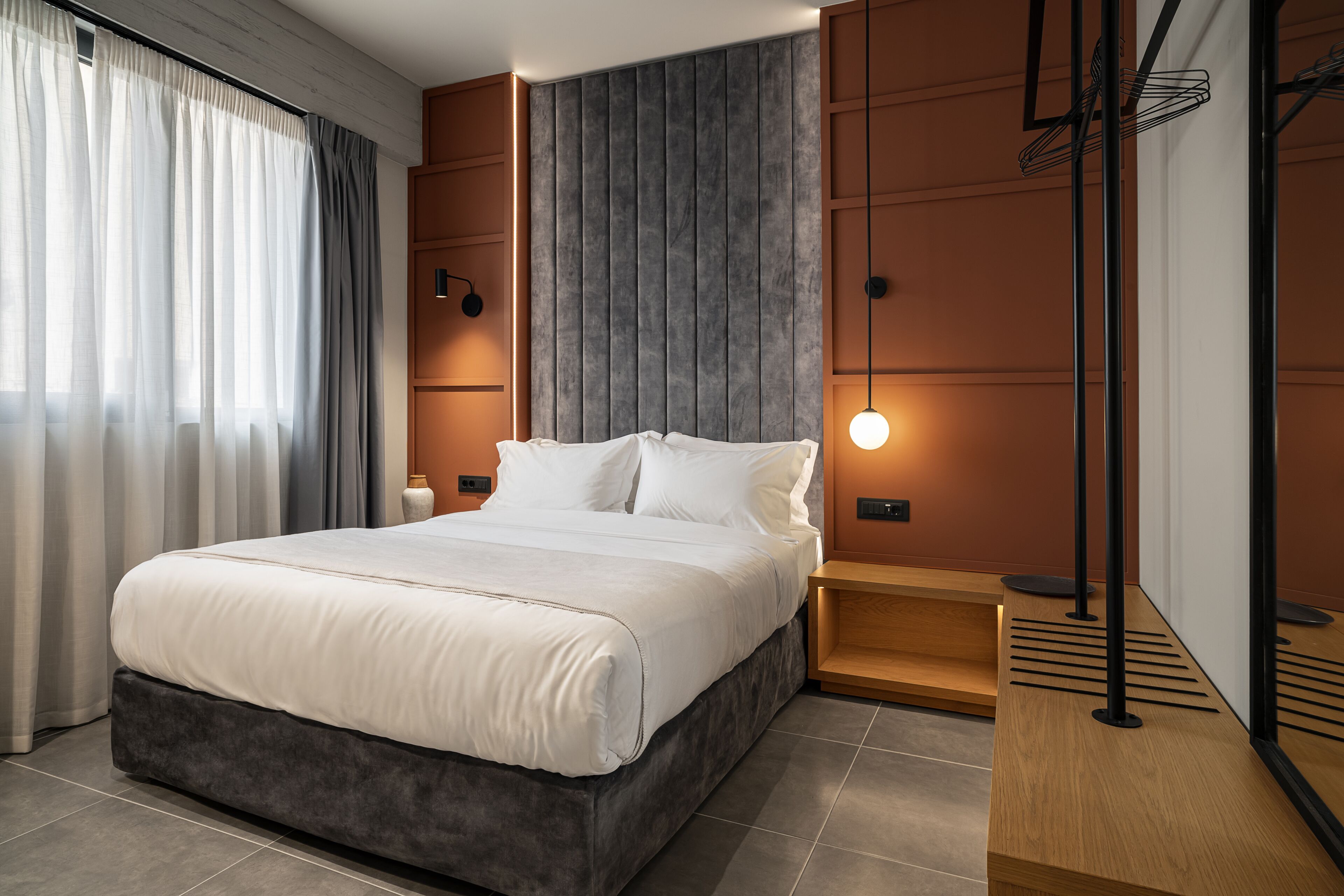 Une chambre à coucher moderne avec un grand lit, une table de chevet, une lampe fixée au mur et une table de nuit en bois.