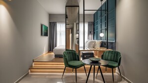 A modern hotel room with a bed, a desk, two chairs, a small table, and a large window with curtains. - Bob W Athens Akadimia (Athens)