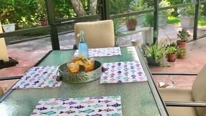 A table with a drink, a bowl, and a patterned placemat in a room with large windows and potted plants outside. - Beautiful Home with Pool - 3 miles from Siesta Key Beach (Sarasota)