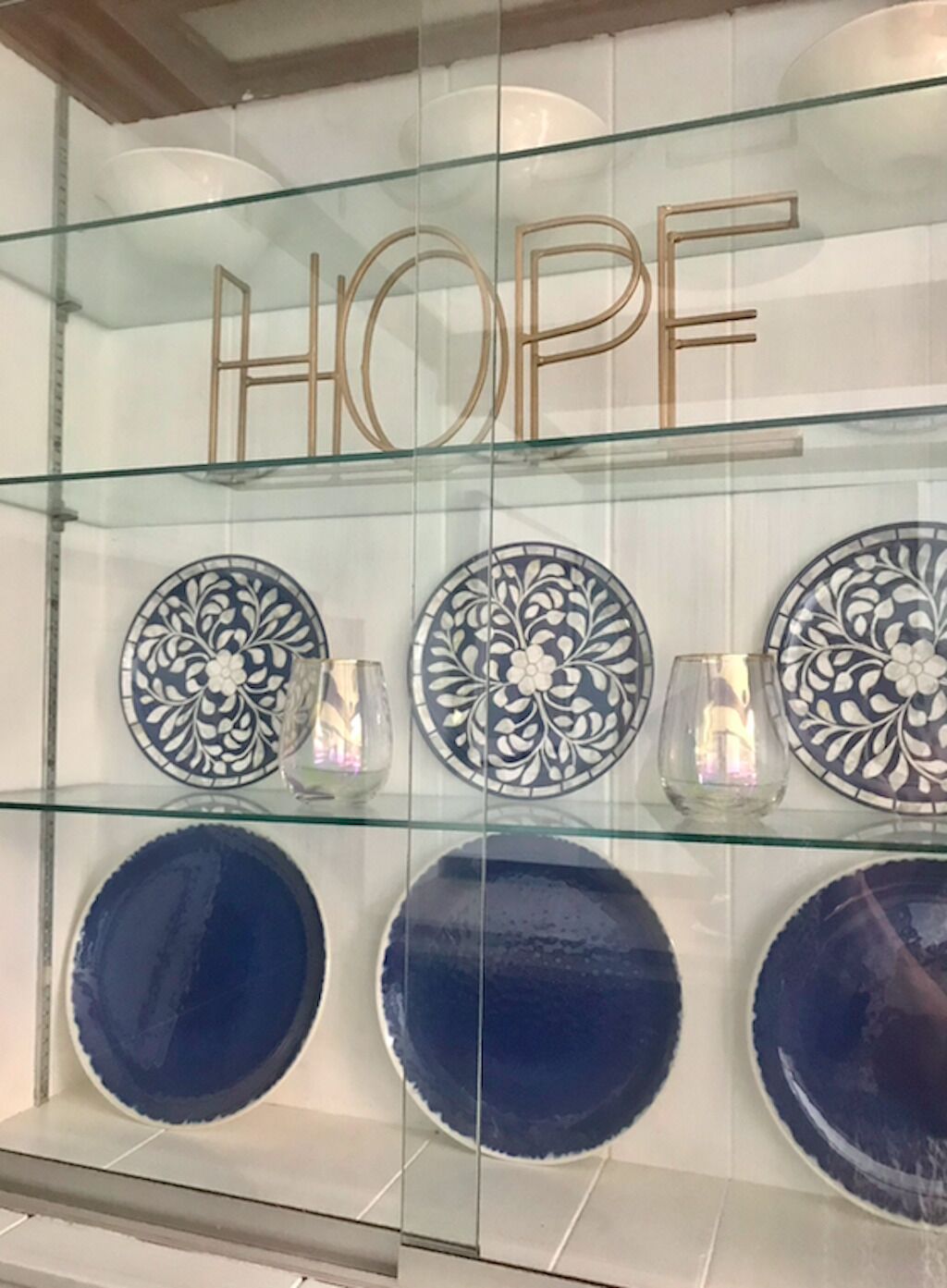 Eine Auswahl dekorativer Teller und ein Glastischchen mit dem Wort 'HOPE' darüber.
