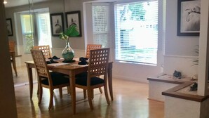 A dining area with a wooden table and chairs, a vase with flowers, and a window with blinds. - Beautiful Home with Pool - 3 miles from Siesta Key Beach (Sarasota)