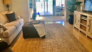 A living room with a sofa, ottoman, and a television on a cabinet. - Beautiful Home with Pool - 3 miles from Siesta Key Beach (Sarasota)