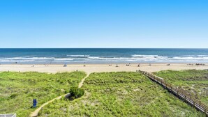 Une plage avec une promenade en bois, des dunes herbeuses et l’océan en arrière-plan.