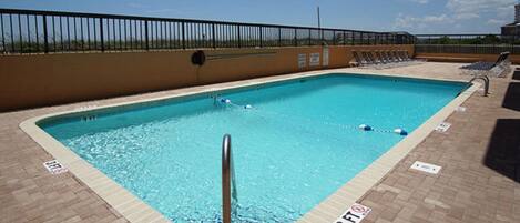 A rectangular pool with a metal safety railing in the foreground, surrounded by a brick deck.