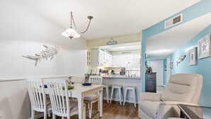 A compact kitchen with white cabinets, a dining area with white chairs, and a light blue accent wall.
