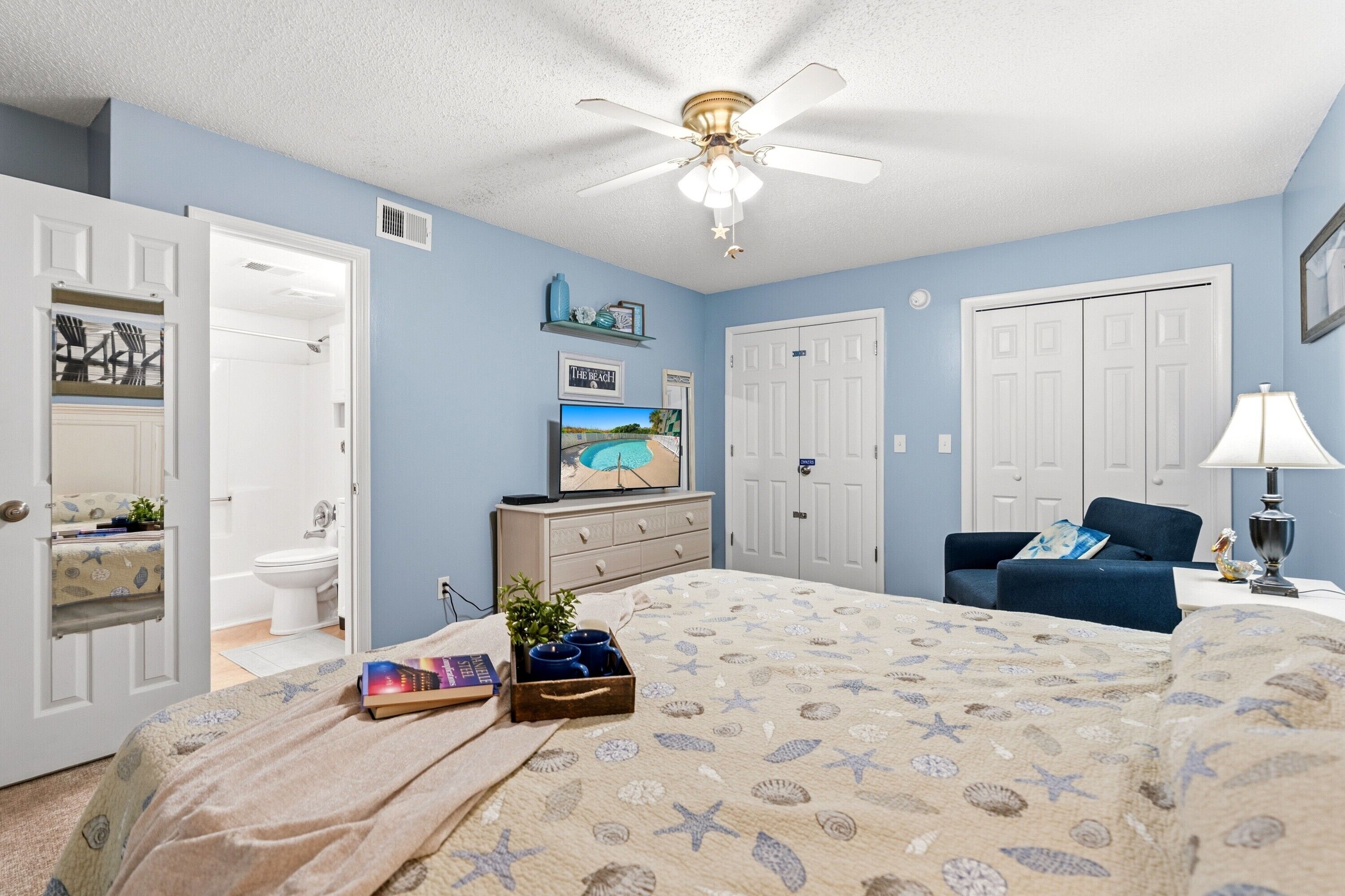 A bedroom with a bed, a ceiling fan, a dresser, a TV, and a chair.