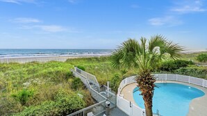 A pool with a palm tree, a beach view, and a staircase leading to a deck.