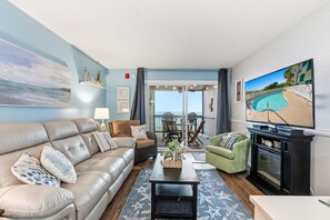 Een woonkamer met een leren bank, een salontafel en een televisie. Er is een balkon met uitzicht op een zwembad.