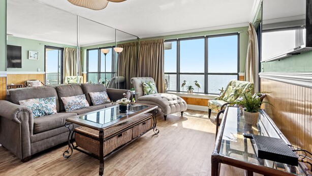 A spacious living room with a sofa, armchairs, a coffee table, and a view of the sea through large windows. - Windemere 1006-3BR Oceanfront Ocean Drive (North Myrtle Beach)