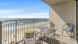 A balcony with a metal table and chairs, overlooking a beach with a clear sky. - Windemere 1006-3BR Oceanfront Ocean Drive (North Myrtle Beach)