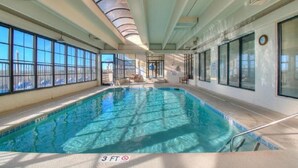 An indoor swimming pool with clear glass walls, a ceiling with a circular design, and a visible clock on the wall. - Windemere 1006-3BR Oceanfront Ocean Drive (North Myrtle Beach)
