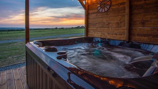 A hot tub with a wooden exterior, a clock on the wall, and a view of a sunset over a field.