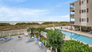 A poolside area with lounge chairs, a pool, and a view of the ocean. - Windsong 106-1BR/1BA Oceanfront condo in Windy Hill (North Myrtle Beach)