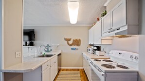 A compact kitchen with white cabinets, a microwave, a stove, and a sink. - Windsong 106-1BR/1BA Oceanfront condo in Windy Hill (North Myrtle Beach)