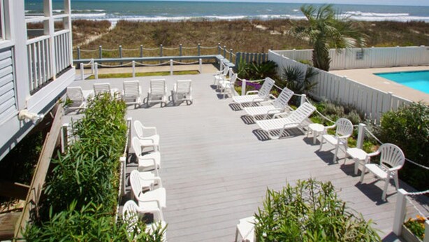 A deck with white lounge chairs and a pool, overlooking the ocean. - Windsong 106-1BR/1BA Oceanfront condo in Windy Hill (North Myrtle Beach)