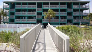 A multi-story building with balconies, a central entrance, and a pathway leading to it. - Windsong 106-1BR/1BA Oceanfront condo in Windy Hill (North Myrtle Beach)