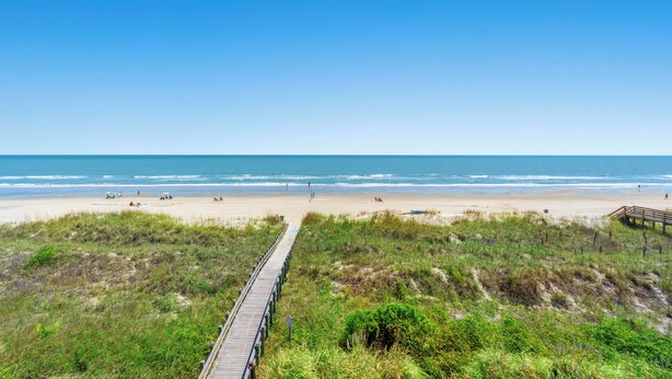 Une plage avec une promenade en bois qui mène au bord de l’eau, entourée de dunes herbeuses.