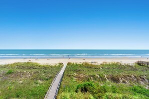 Ein Strand mit einer Holzpromenade, die zum Ufer führt, umgeben von grasbewachsenen Dünen.