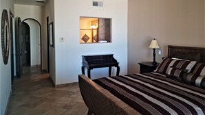 A hotel room with a bed, a desk, a lamp, and a mirror. There is a hallway leading to another room. - Luxury Three Bedroom Ocean Front Condominium (San Felípe)