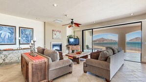 A spacious living room with a sofa set, a coffee table, and a television. There is a balcony with a view of mountains. - Luxury Three Bedroom Ocean Front Condominium (San Felípe)