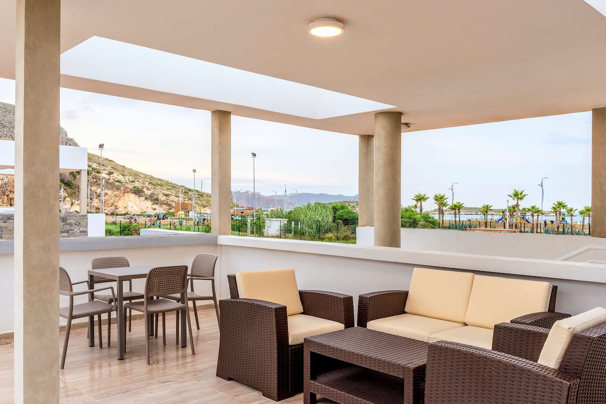 A covered outdoor seating area with wicker furniture and a view of a coastal landscape.