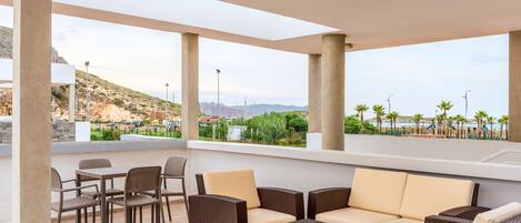 A covered outdoor seating area with wicker furniture and a view of a coastal landscape.