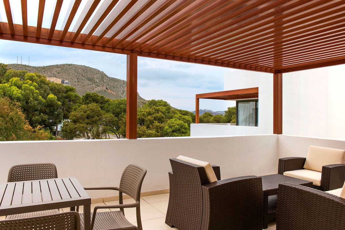 A covered outdoor seating area with wicker furniture and a view of a mountainous landscape.