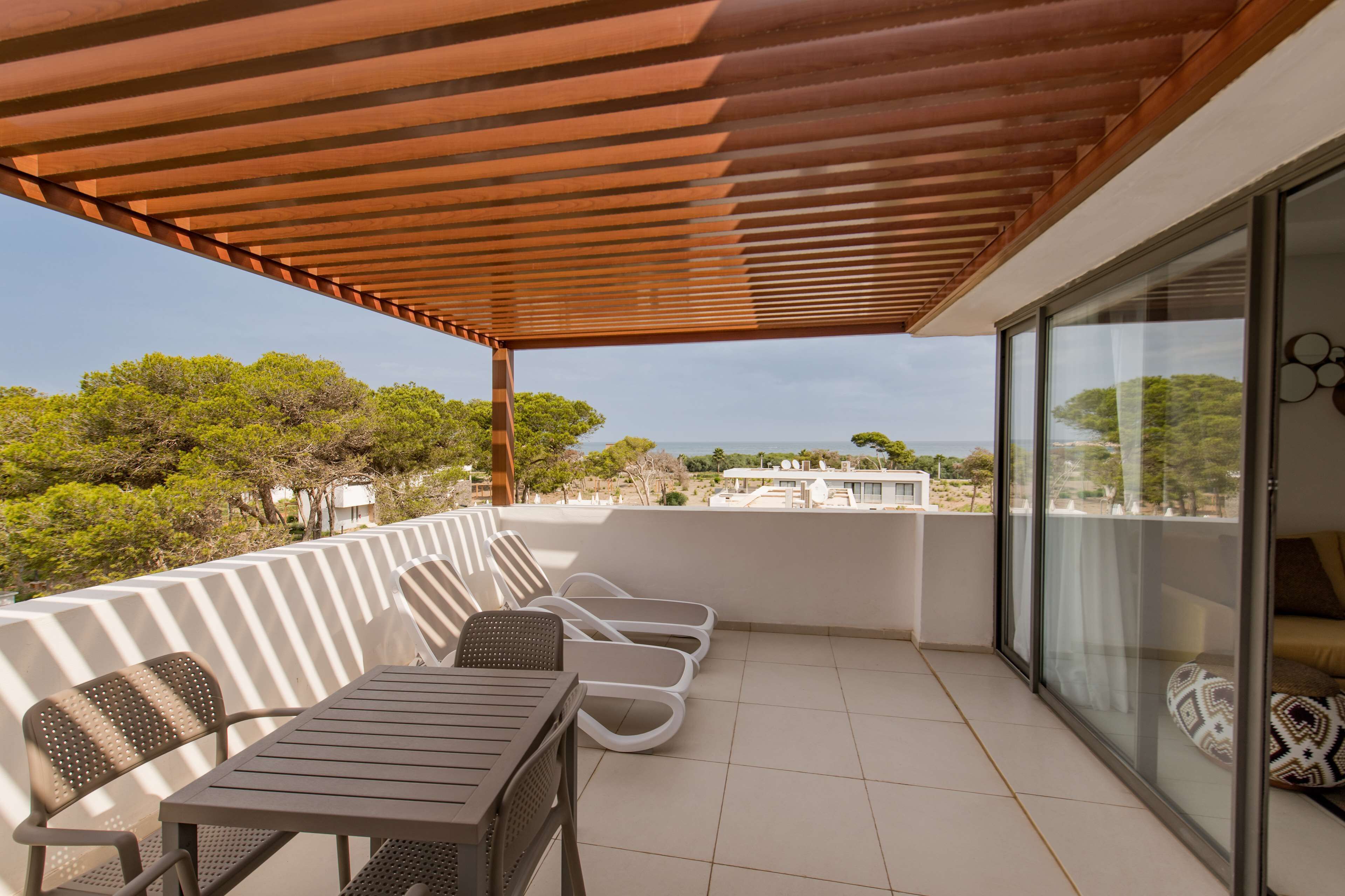 A covered outdoor seating area with a table and chairs, overlooking a scenic view of trees and buildings.