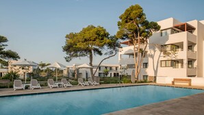 A swimming pool with lounge chairs and a wooden bench, surrounded by modern buildings and trees. - Radisson Blu Residences Al Hoceima (Ait Youssef Ou Ali)