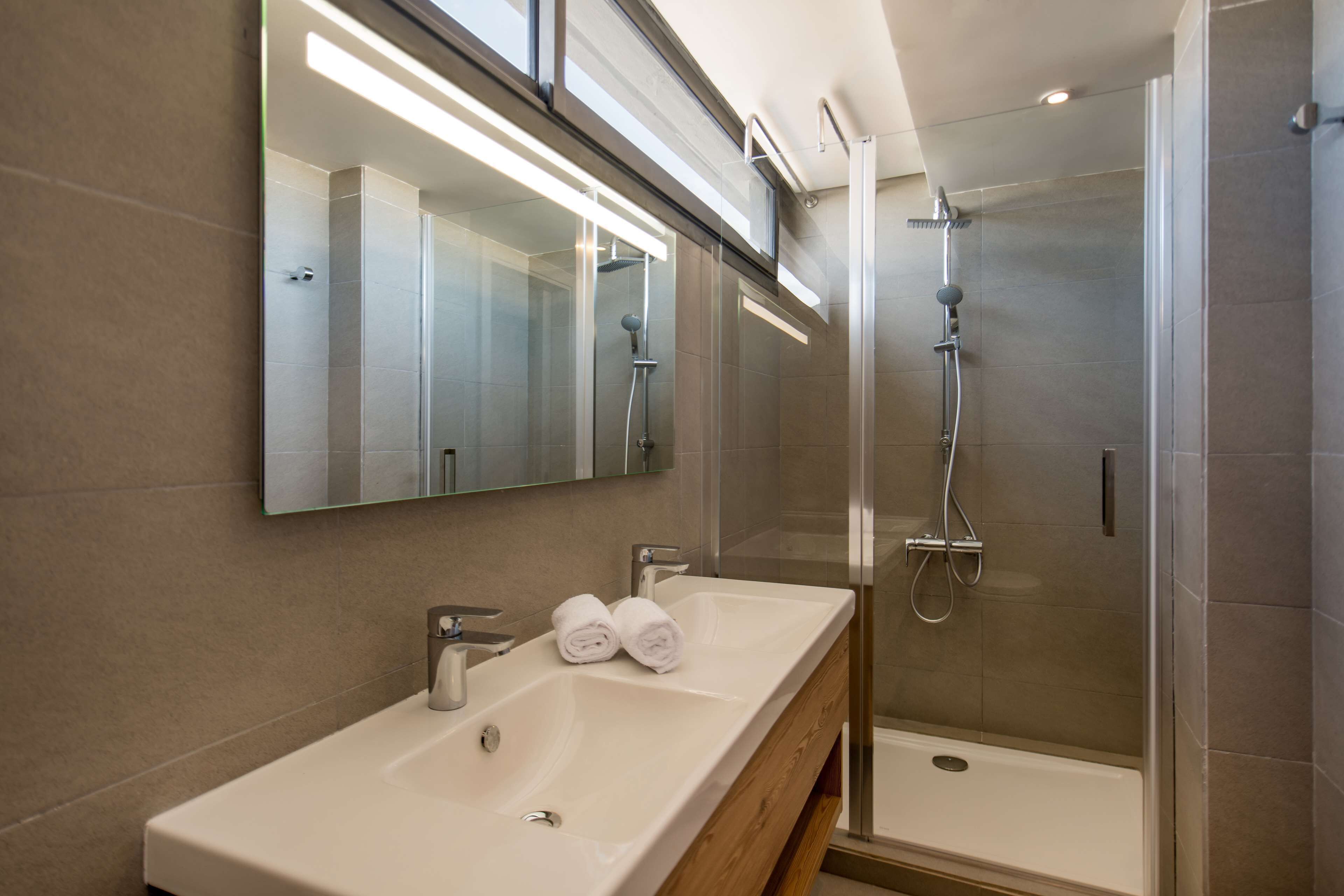 A modern bathroom with a large mirror, two sinks, and a glass-enclosed shower.