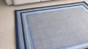 Ein beiges Sofa mit einer blau-weißen Decke, einem blau-weiß gestreiften Teppich und einer Wand mit einem Kunstwerk von einer Möwe.