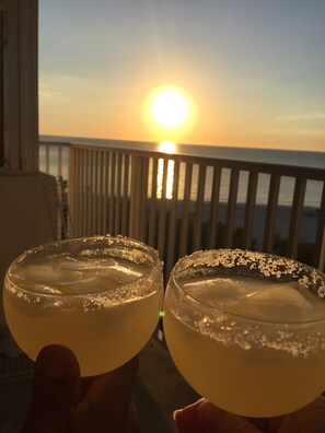 TvÄ drinkar med salt pÄ glaskanten, serverade pÄ en balkong med en solnedgÄng i bakgrunden.