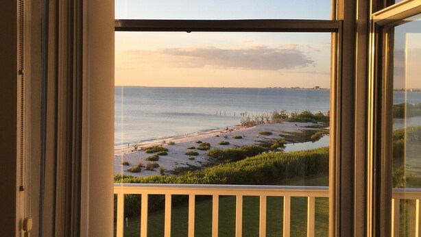 Blick aus einem Fenster auf einen Strand und ein Gewässer.