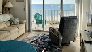 Ein Hotelzimmer mit einer großen Schiebeglasdoor, die auf einen Balkon mit Meerblick führt. Es gibt ein Bett, einen Sessel und einen Schreibtisch mit einem Computer.