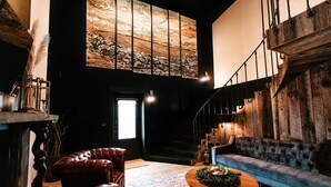 A spacious living area with a high ceiling, a large wall mural, a staircase, and a blue sofa.
