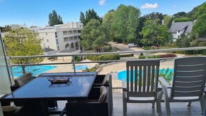 Ein Balkon mit Tisch und Stühlen, mit Blick auf einen Swimmingpool und umliegendes Grün.