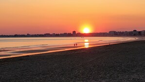 Ein Strand bei Sonnenuntergang mit klarem Himmel, ruhiger See und Gebäuden in der Ferne.