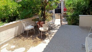 Une terrasse avec une table et des chaises, entourée de verdure et dotée d’un sol en gravier.