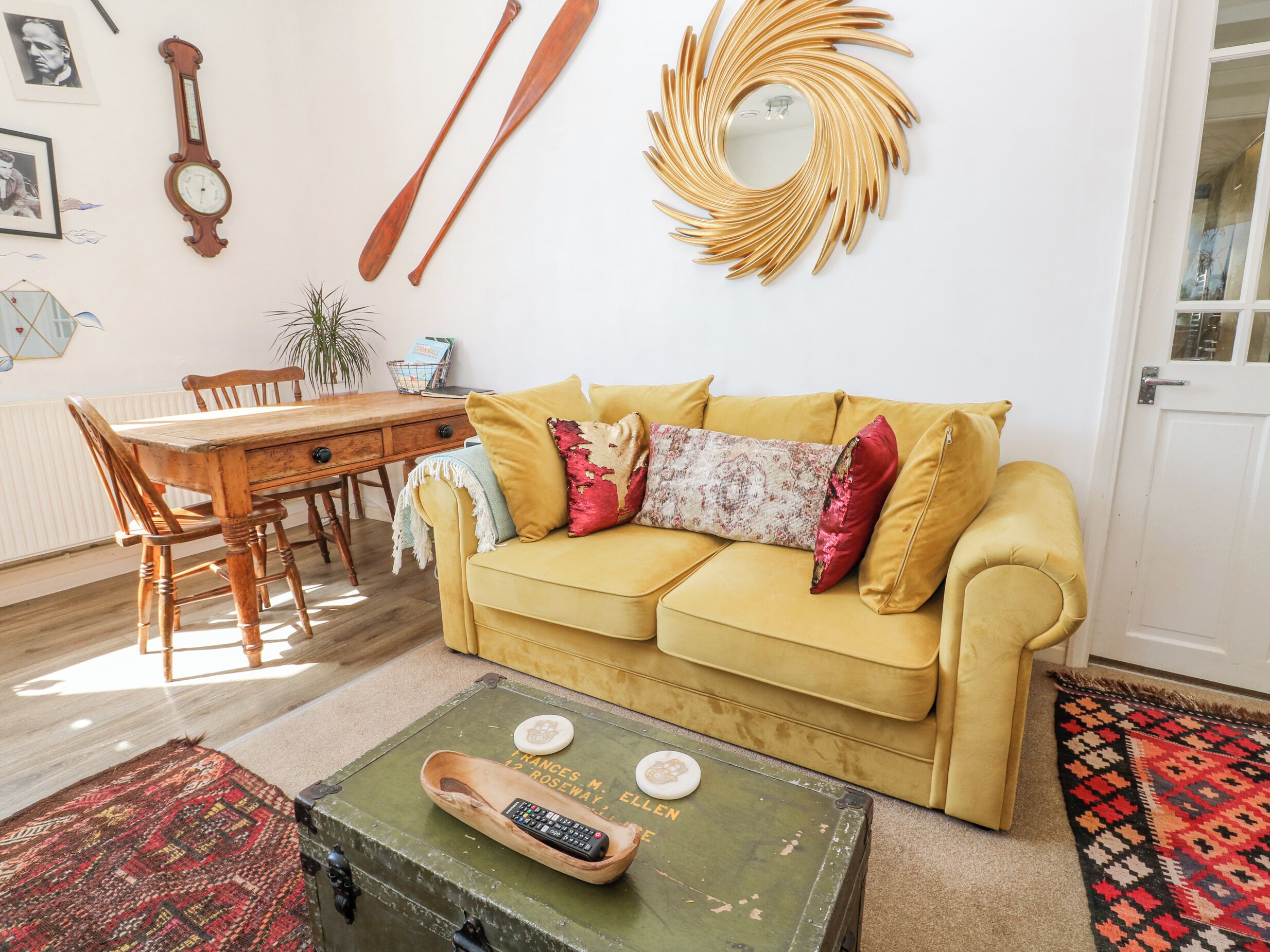 Un salón con sofá amarillo, mesa de centro de madera y un baúl verde con un control remoto.