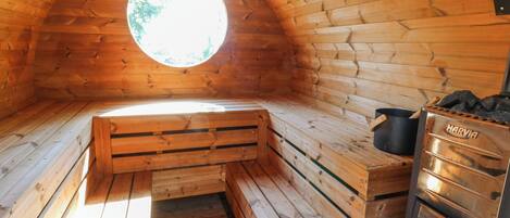 Interior de una cabaña de madera con sauna integrada, una ventana y un horno Harvia de leña.