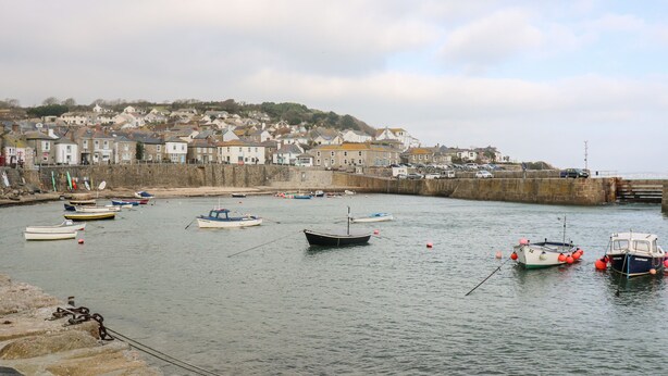 A harbor with boats docked, a stone wall, and houses in the background. - The Cottage (Penzance)